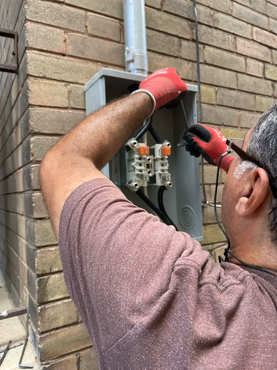 Electrician working on an outdoor meter base and disconnect on a brick wall in Thornhill